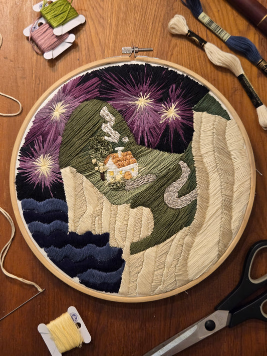 Embroidery hoop with a colorful stitched design on a wooden surface with embroidery tools.