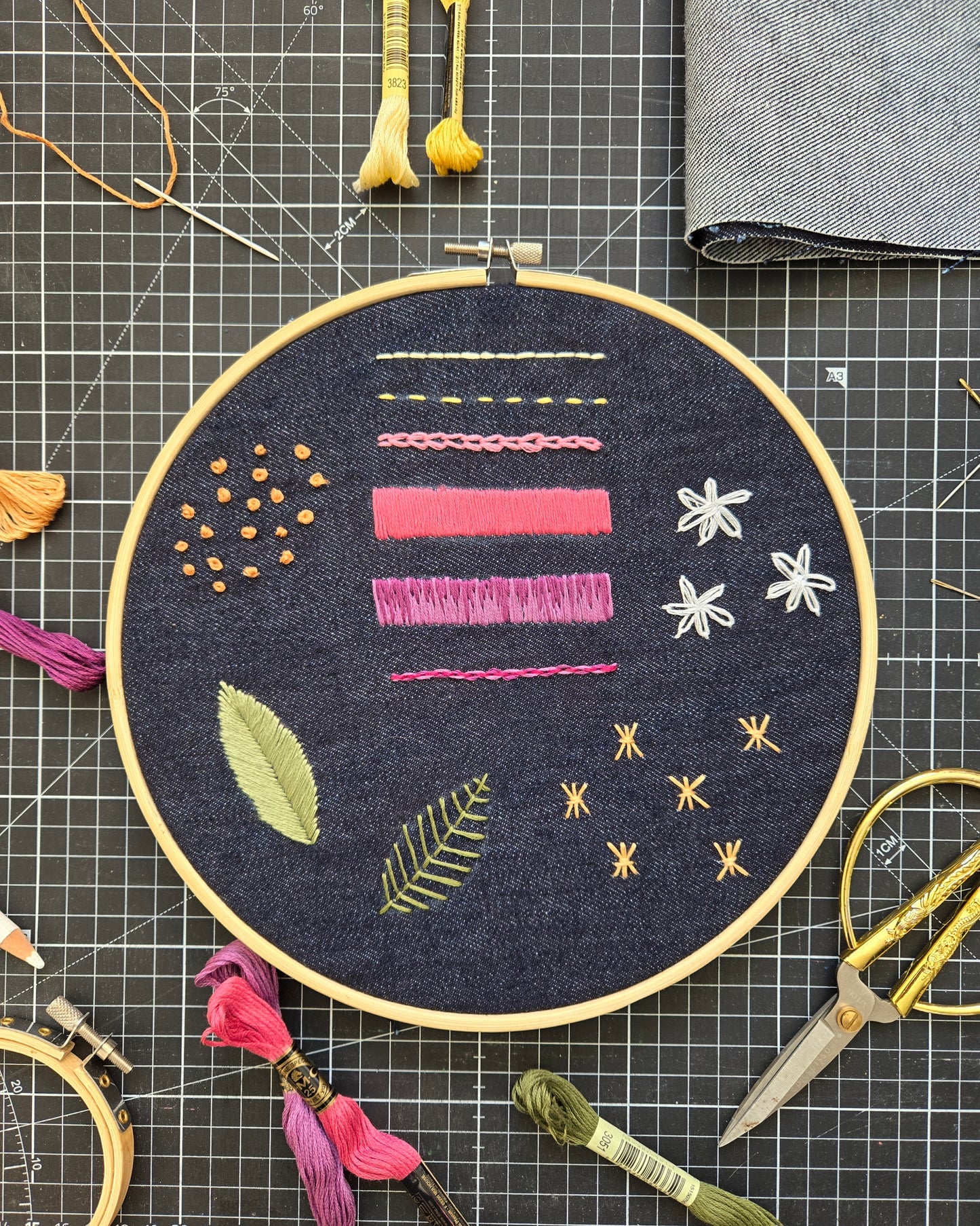 Embroidery hoop with colorful patterns on a grid surface with sewing tools.